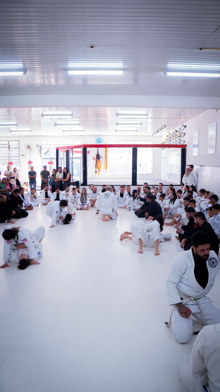 Turma reunida sentada no tatame durante a aula, adultos e crianças de kimono